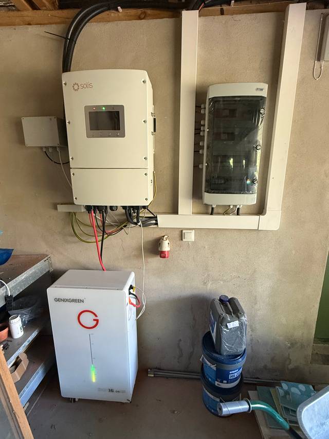 Falownik, rozdzielnica i biały magazyn energii ustawiony przy ścianie w garażu.